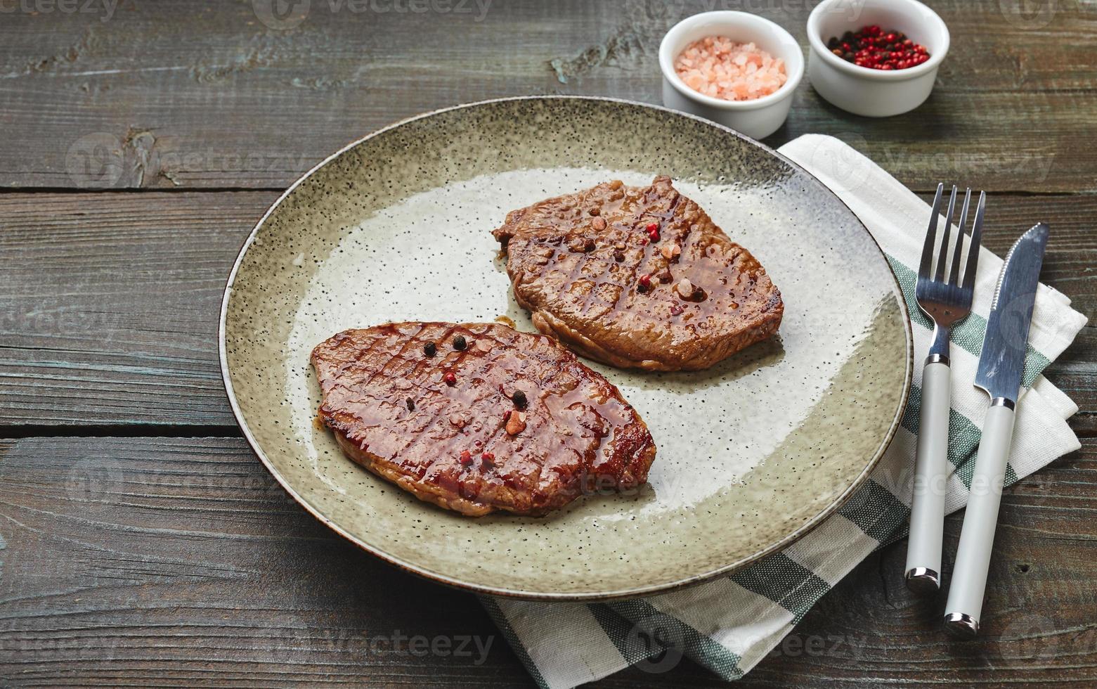 twee gegrild biefstuk steaks, specerijen en tomaat-komkommer salade met verzuren room Aan een houten tafel. foto