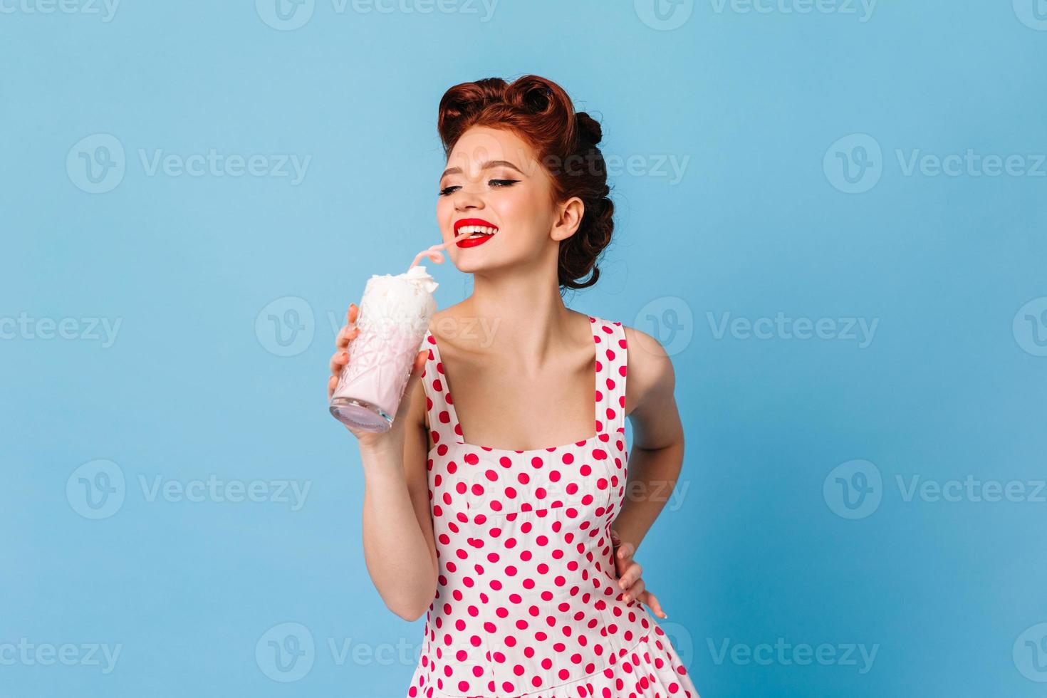 geïnspireerd meisje in stip jurk drinken milkshake. lachend gember vrouw model- Holding drank foto