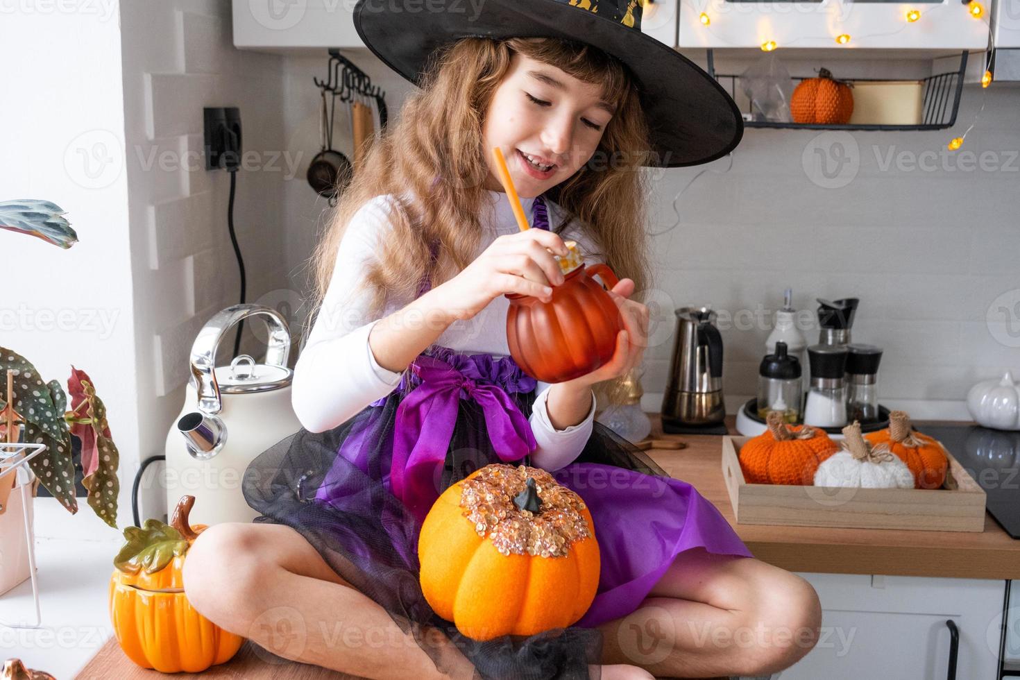 kind drankjes pompoen sap, groente smoothie of cocktail van een mok met een rietje. keuken siert voor halloween. meisje in een heks kostuum. herfst knus in huis foto