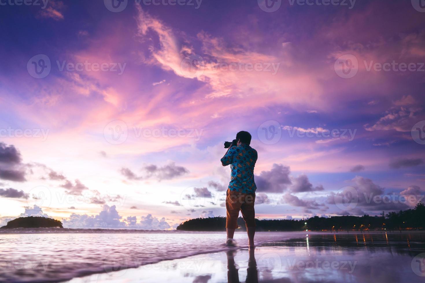 achterzijde visie van volwassen reizen Aziatisch fotograaf Mens met camera Aan strand zand met mooi dramatisch zonsondergang lucht foto