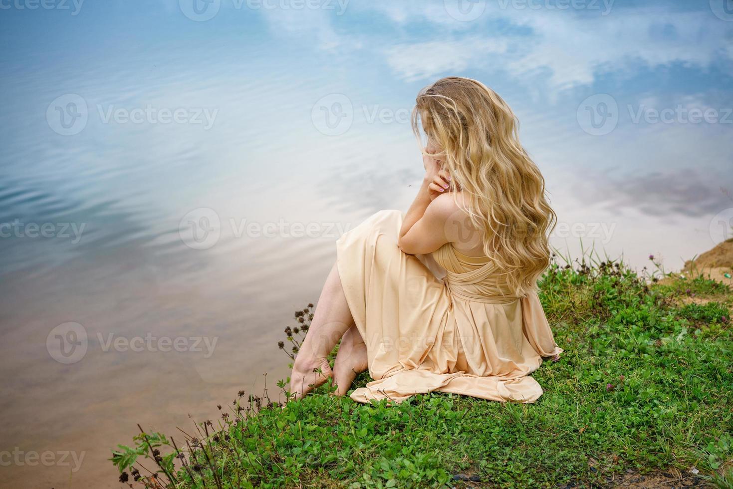 mooi verdrietig meisje zittend Aan de kust van de meer in een jurk , de concept van eenzaamheid foto