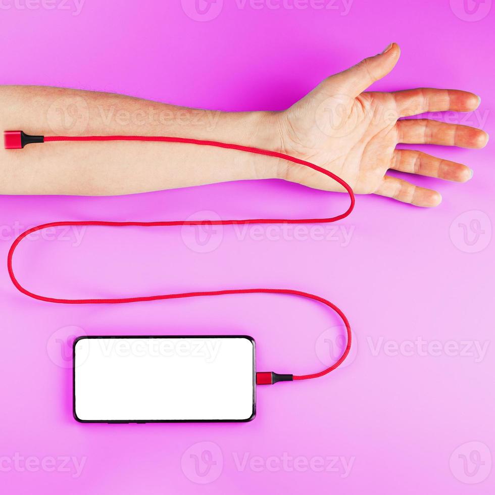 een smartphone met een groot wit scherm is verbonden via een rood USB koord naar een ader in de hand- Aan een roze achtergrond. foto