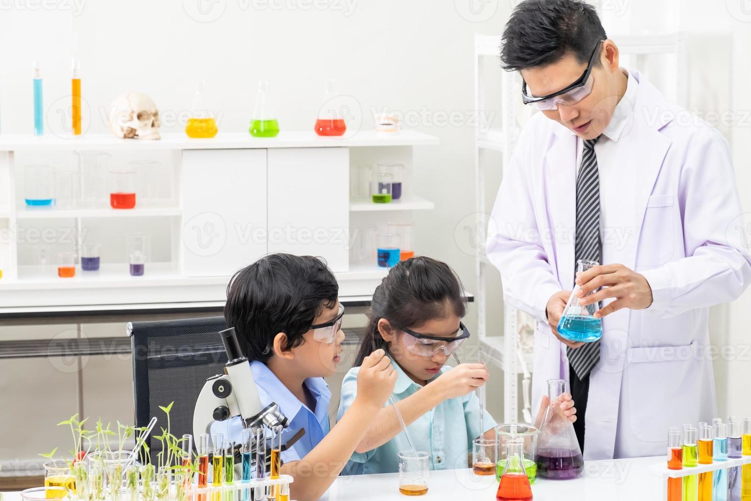 jong Aziatisch jongen en meisje glimlach en hebben pret terwijl aan het doen wetenschap experiment in laboratorium klas met docent. studie met wetenschappelijk uitrusting en buizen. onderwijs concept. foto