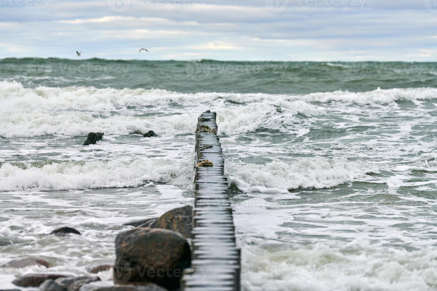 uitzicht op blauwe zee met schuimende golven en houten golfbrekers foto