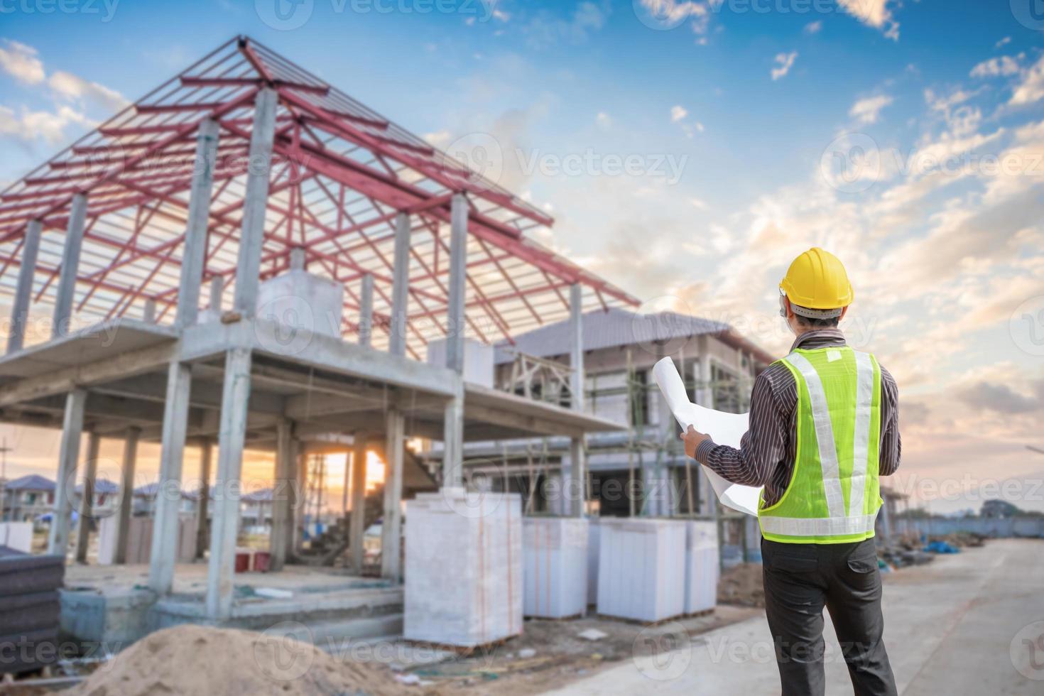 jong professioneel ingenieur in beschermend helm en blauwdrukken papier Bij de huis gebouw bouw plaats foto