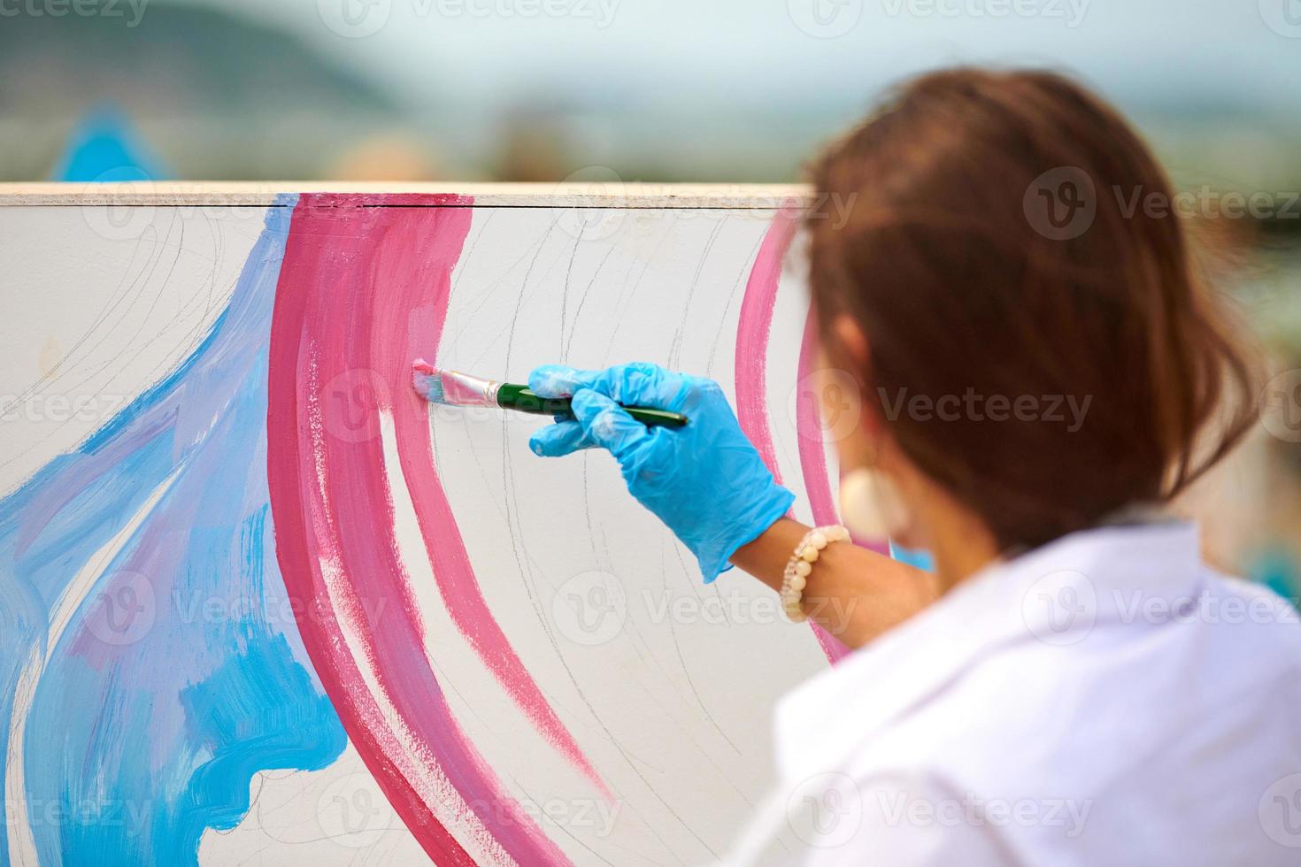 vrouw artiest werken Aan abstract olie schilderij buitenshuis, hand- Holding verf borstel, groot canvas foto