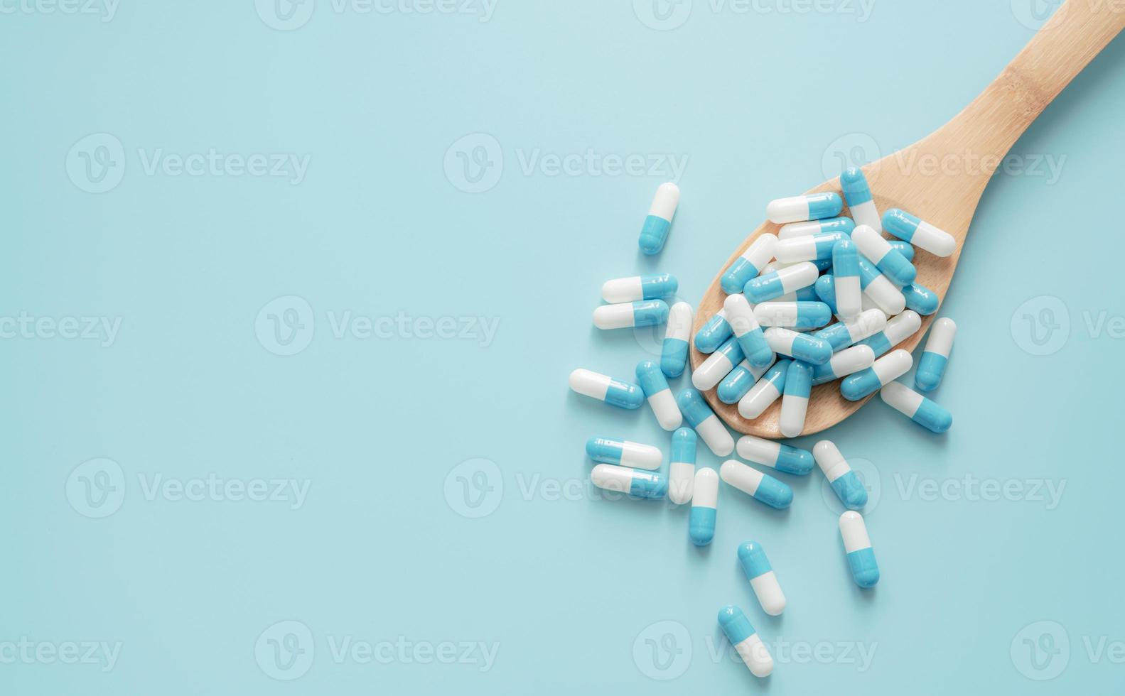 top visie van blauw Wit antibiotica capsule pillen Aan houten lepel en blauw achtergrond. antibiotica drug weerstand. voorschrift medicijn. medisch zorg. farmaceutisch zorg. antimicrobieel drug overmatig gebruik. foto