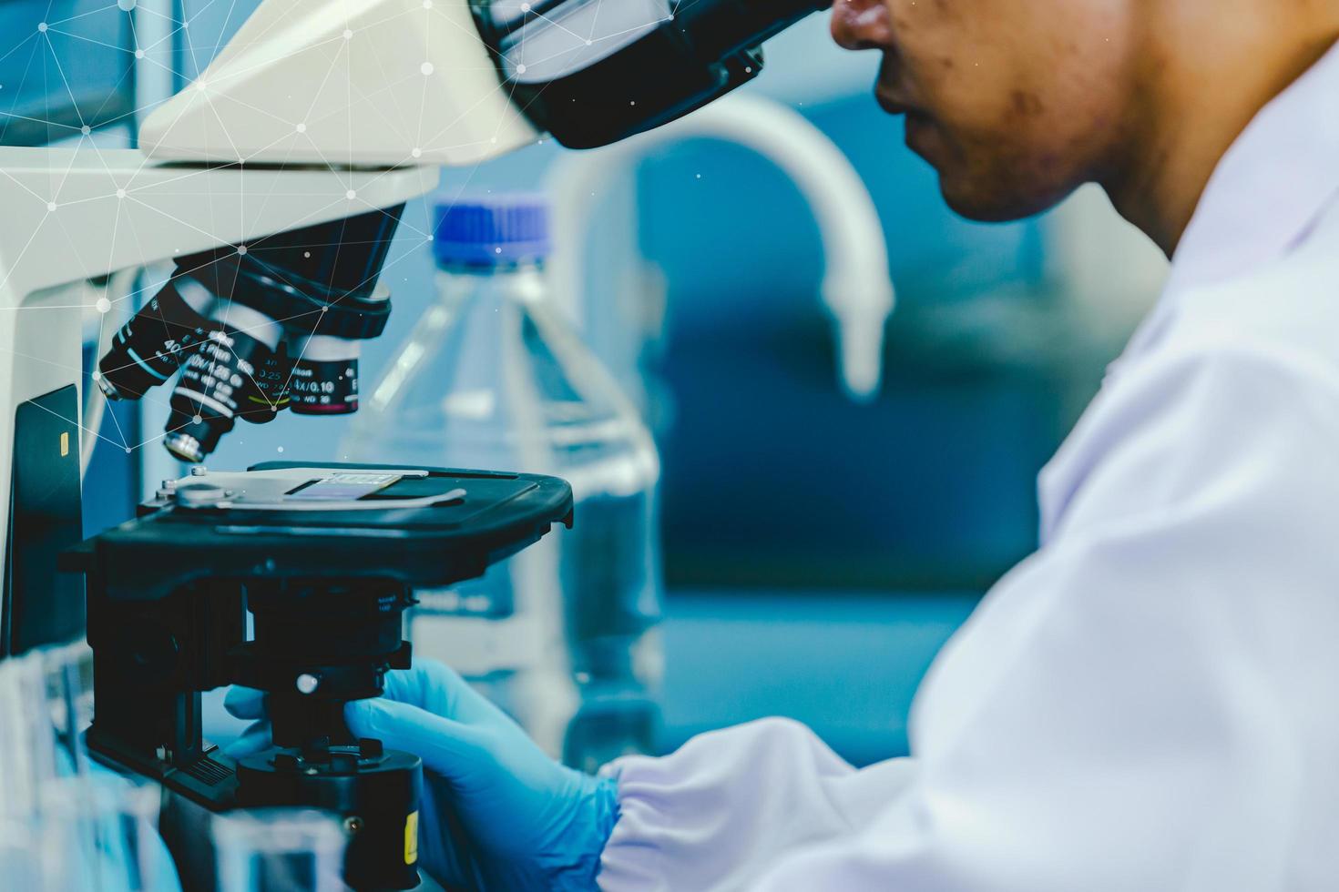 Aziatisch mannetje medisch of wetenschappelijk onderzoeker of dokter gebruik makend van op zoek Bij een Doorzichtig oplossing in een laboratorium. foto