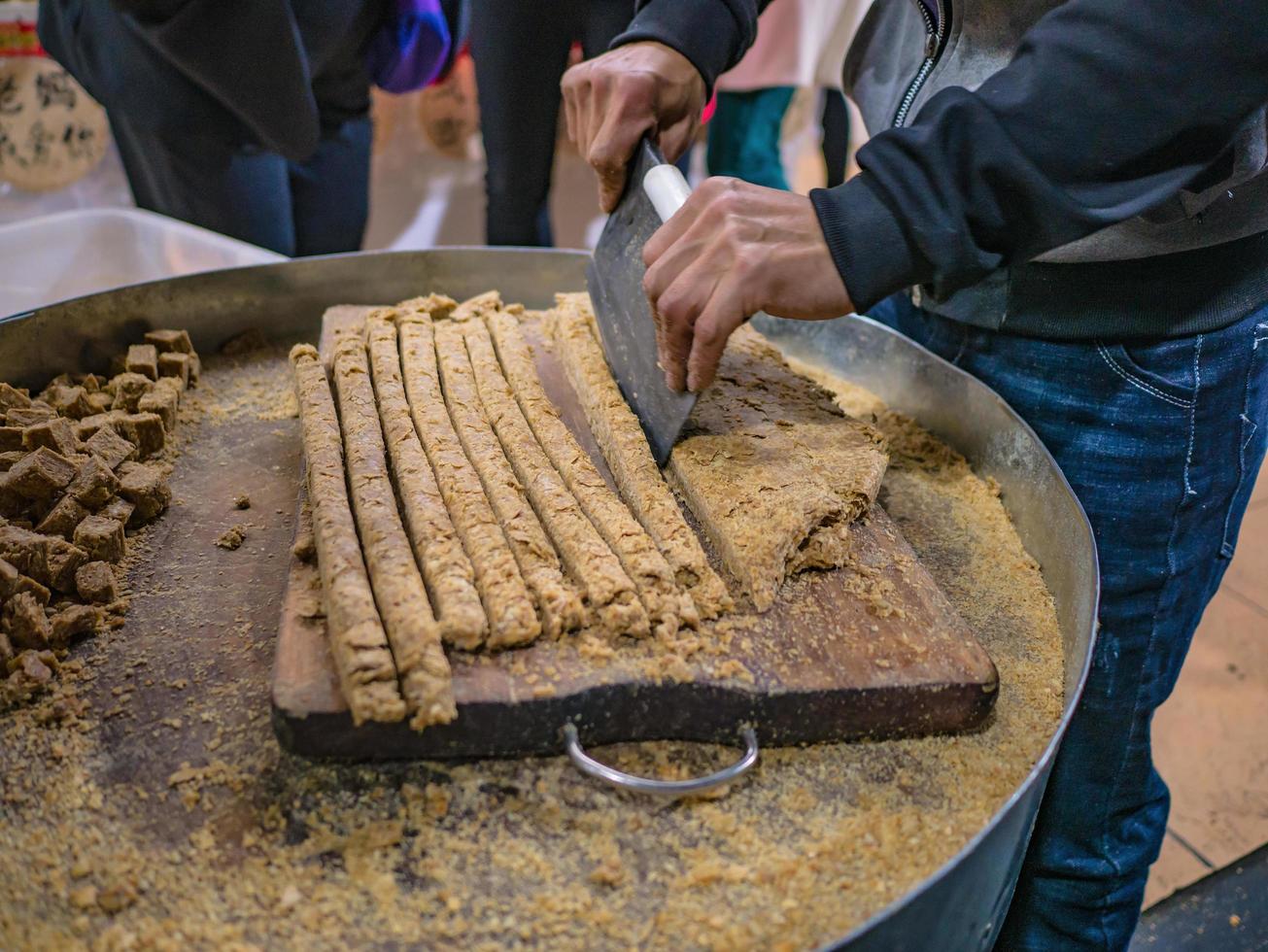 snijdend zoet pinda's stok met knap mes in souvenir winkel van fenghuang oud stad- foto