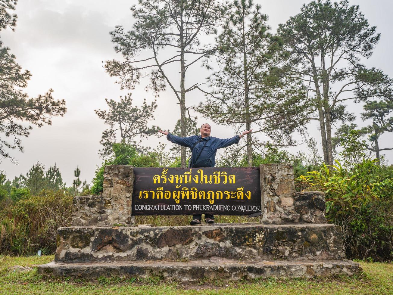 Aziatisch reiziger met felicitatie naar phukradueng veroveraarteken Aan de top van phu kradueng berg nationaal park in loei stad thailand.phu kradueng berg nationaal park beroemd reizen bestemming foto