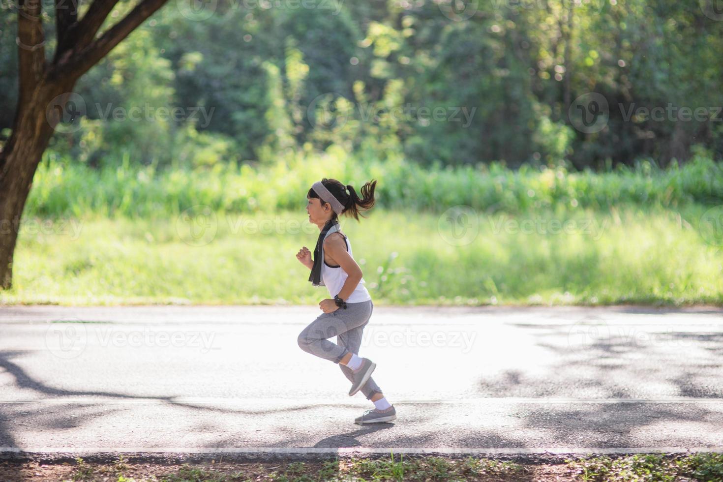 gelukkig kind meisje rennen in de park in zomer in natuur. warm zonlicht gloed. Aziatisch weinig is rennen in een park. buitenshuis sport- en fitheid, oefening en wedstrijd aan het leren voor kind ontwikkeling. foto