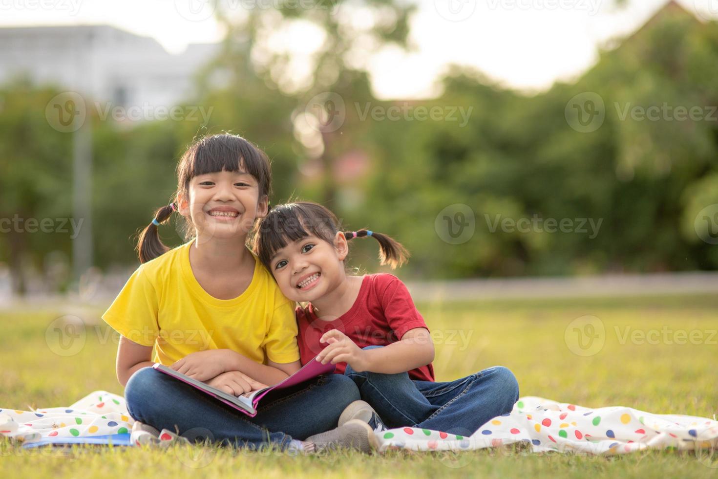 twee mooi weinig meisjes lezing boeken in de tuin , zittend Aan gras. de concept van onderwijs en vriendschap. foto