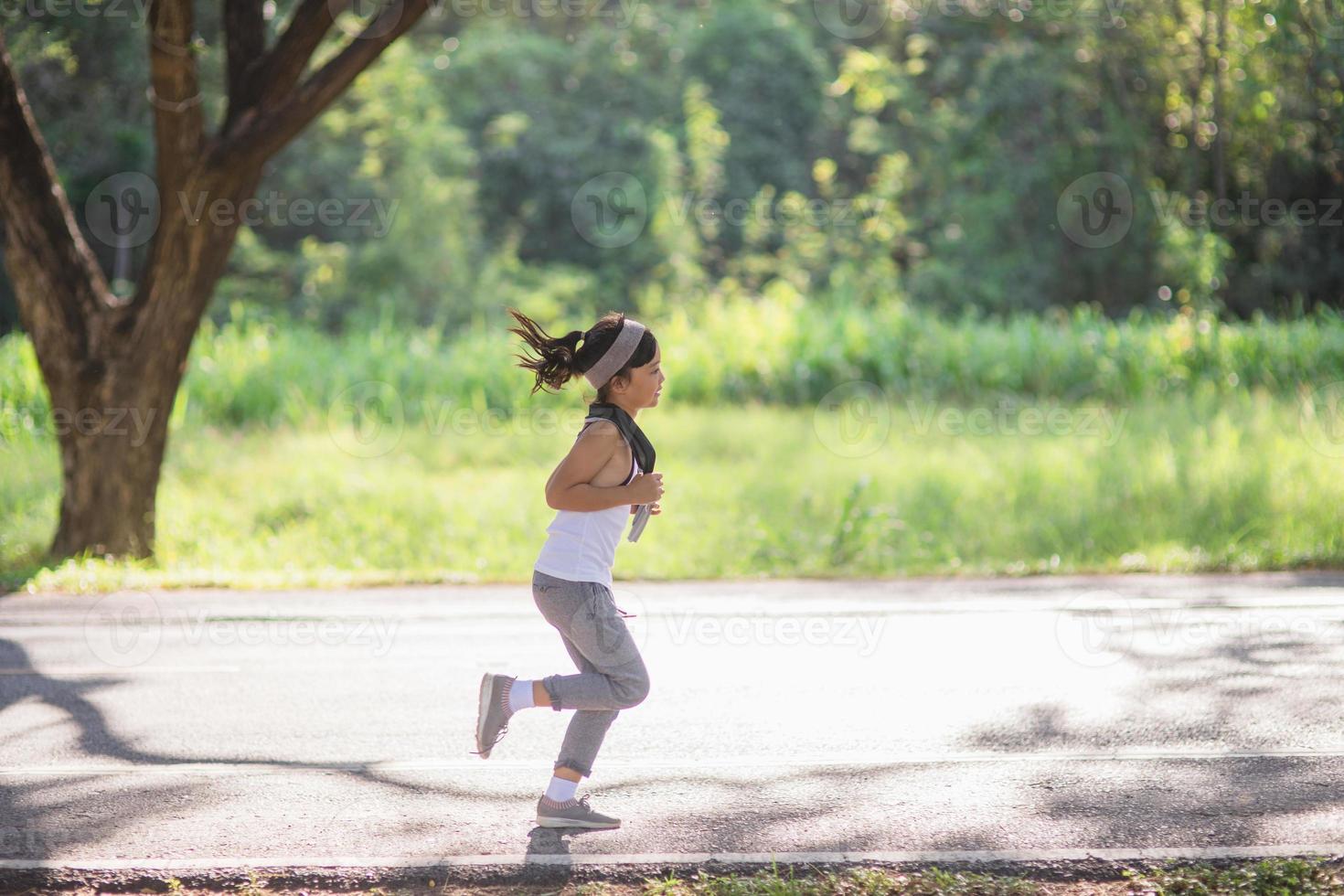 gelukkig kind meisje rennen in de park in zomer in natuur. warm zonlicht gloed. Aziatisch weinig is rennen in een park. buitenshuis sport- en fitheid, oefening en wedstrijd aan het leren voor kind ontwikkeling. foto