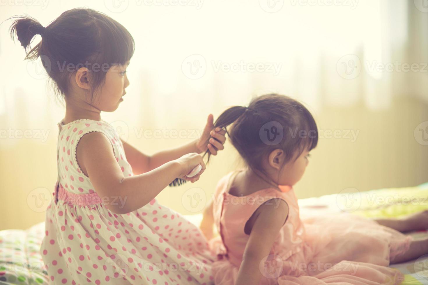 lief weinig meisje poetsen haar- van haar zus terwijl zittend Aan de bed foto