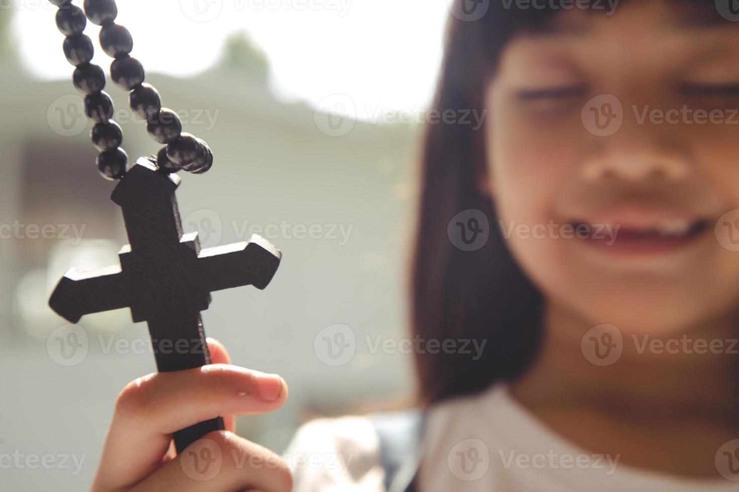 weinig Aziatisch meisje bidden met Holding de kruis, christen concept. foto