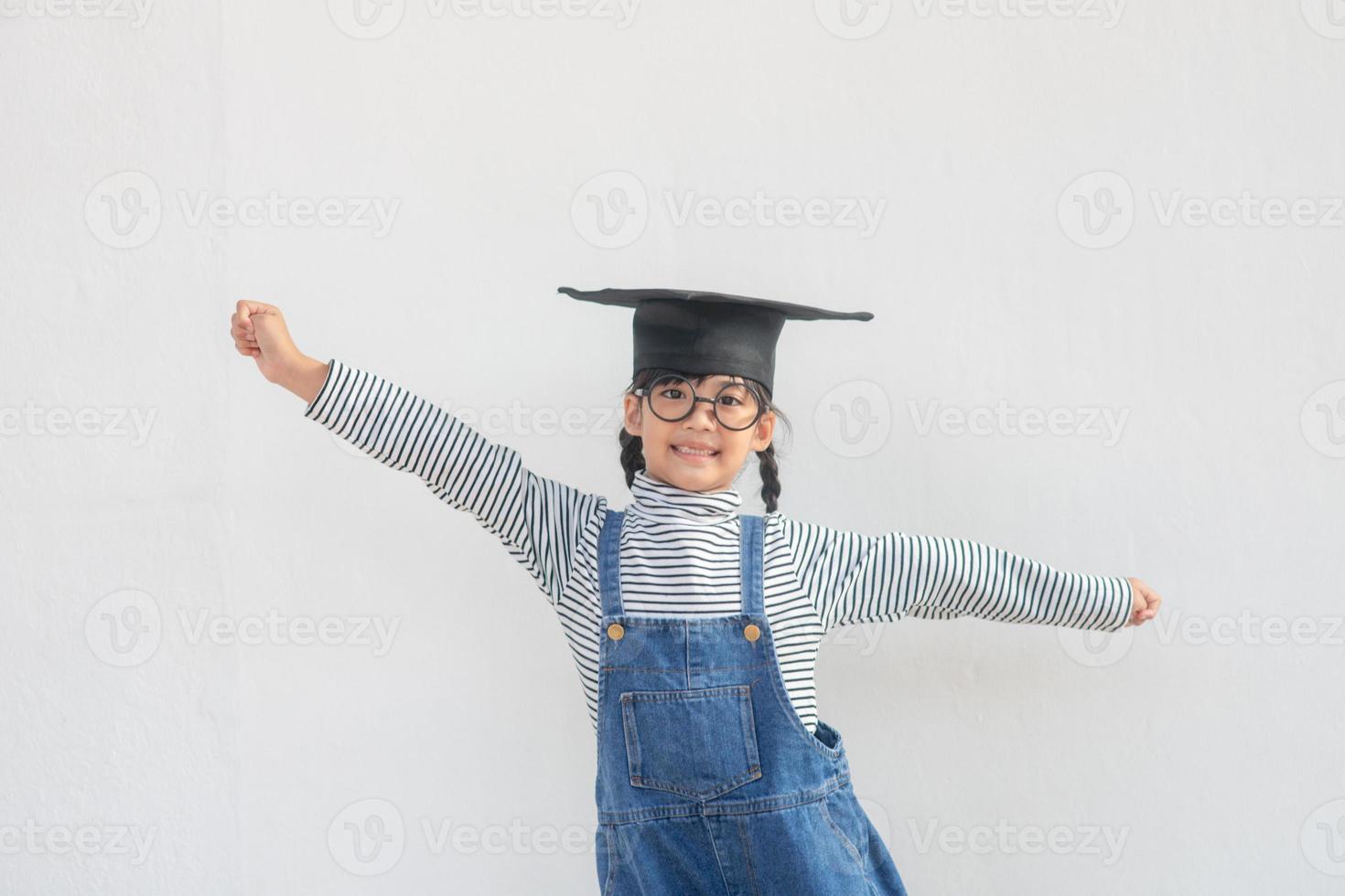 kinderen meisje vervelend een afstuderen pet over- wit achtergrond heel gelukkig en opgewonden aan het doen winnaar gebaar met armen opgevoed, glimlachen en schreeuwen voor succes. viering concept. foto