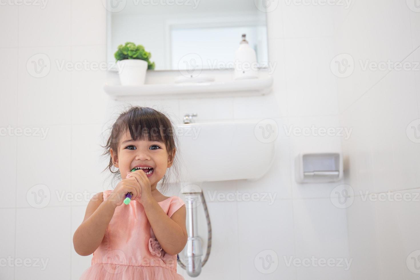 klein schattig babymeisje dat haar tanden schoonmaakt met tandenborstel in de badkamer foto