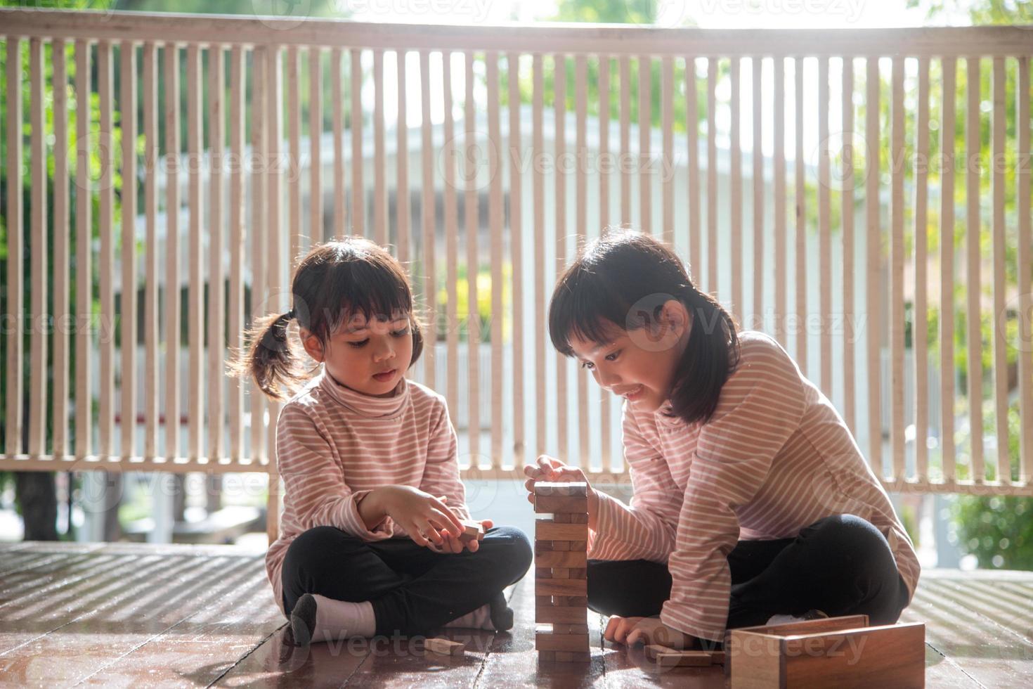 twee Aziatisch meisjes spelen houten stapels Bij huis foto