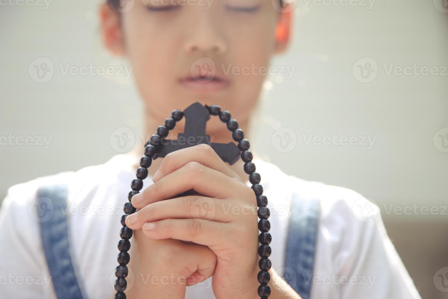 weinig Aziatisch meisje bidden met Holding de kruis, christen concept. foto