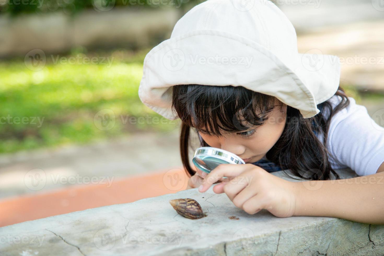 gelukkig kind meisje verkennen natuur met een vergroten glas en een slak. hij hebben pret in de tuin. de concept van de kind is klaar naar Gaan naar school. foto