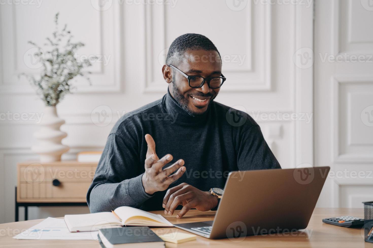 Afro-Amerikaanse jonge zakenman in glazen die online conferentie heeft met werknemers via videogesprek foto