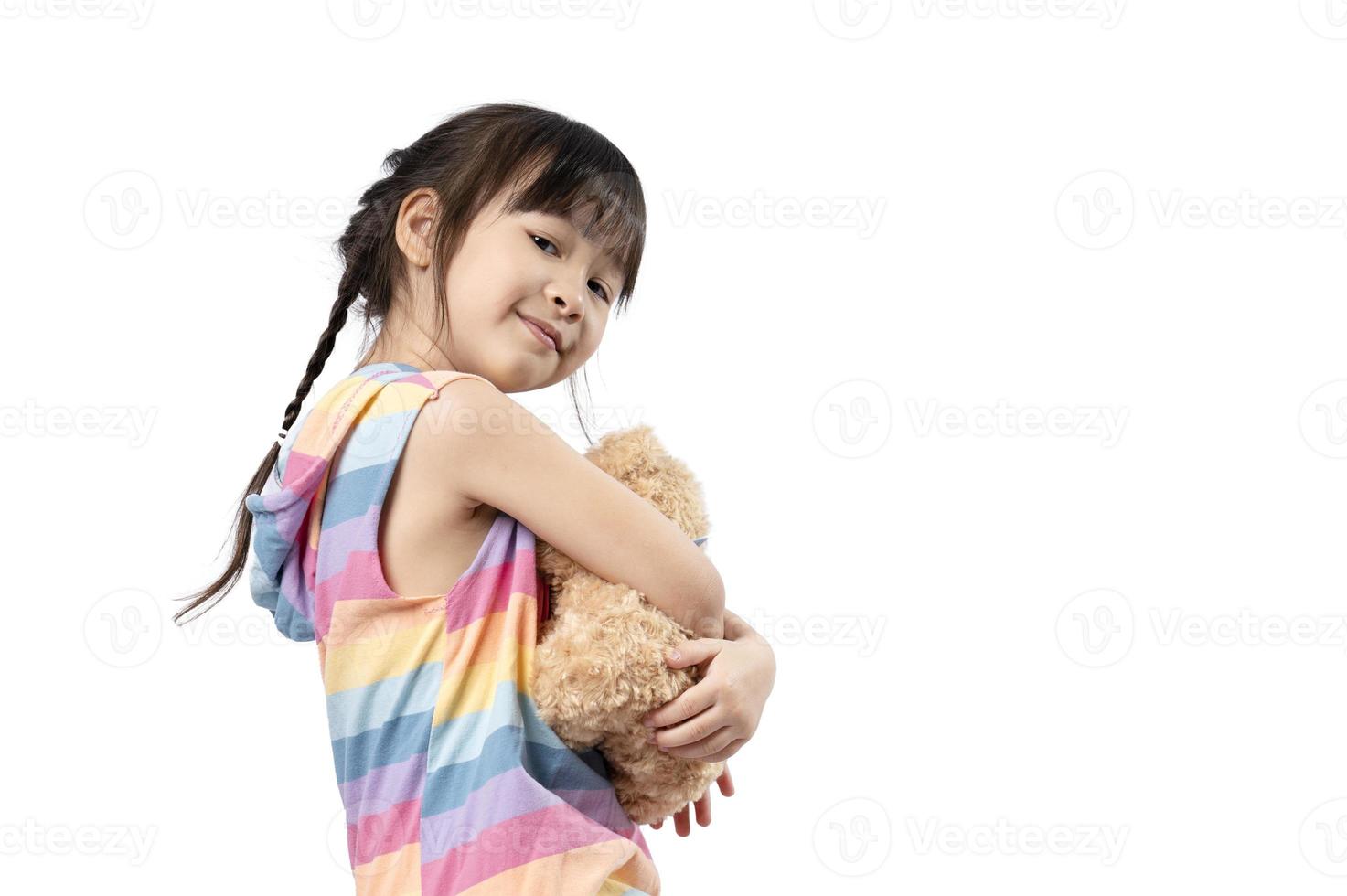 schattig weinig Aziatisch meisje knuffelen haar favoriete bruin teddy beer en glimlachen in wit achtergrond. meisje en pop, favoriete speelgoed, gelukkig kind foto