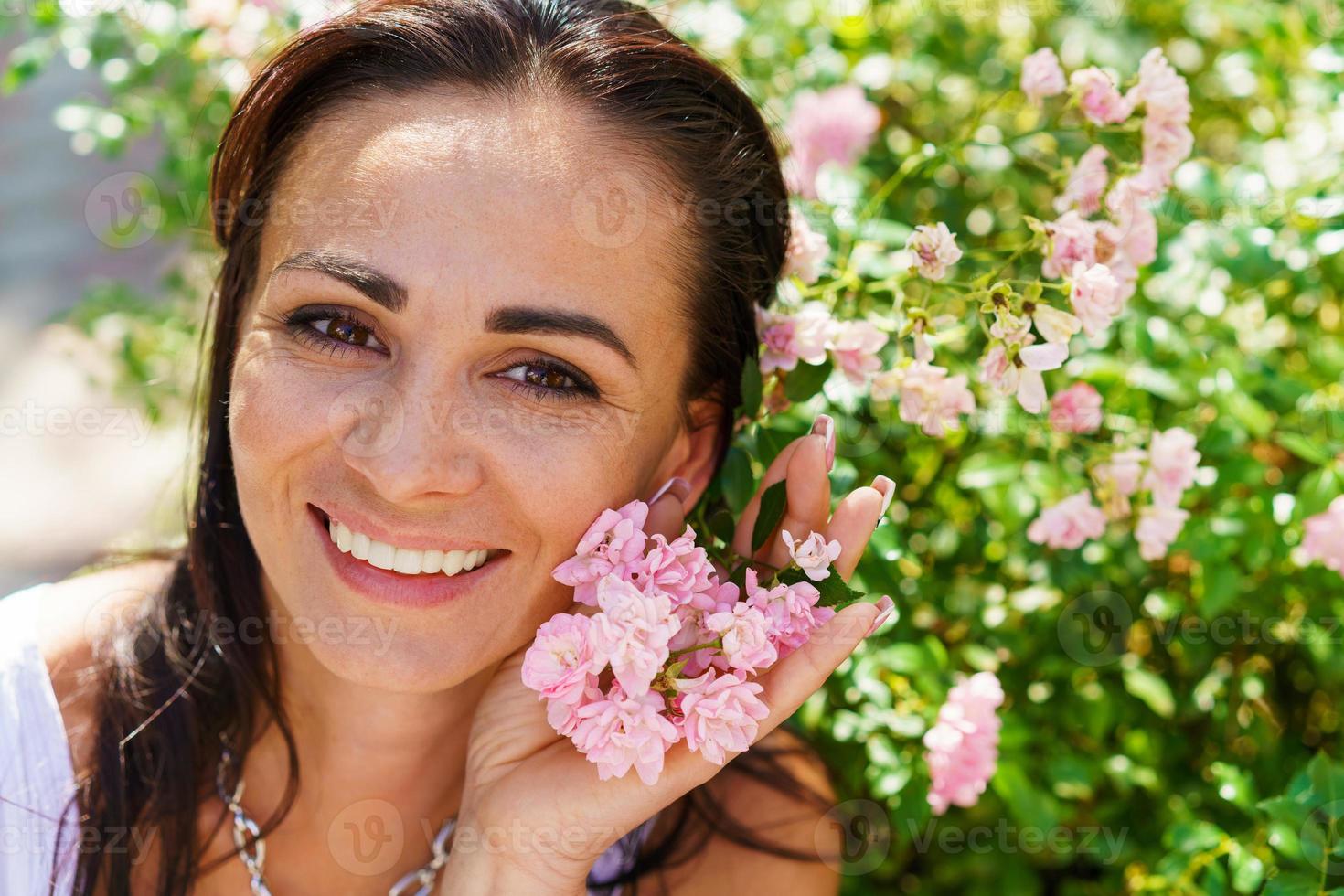 detailopname portret mooi vrouw in park met bloeiend klein roze rozen. foto