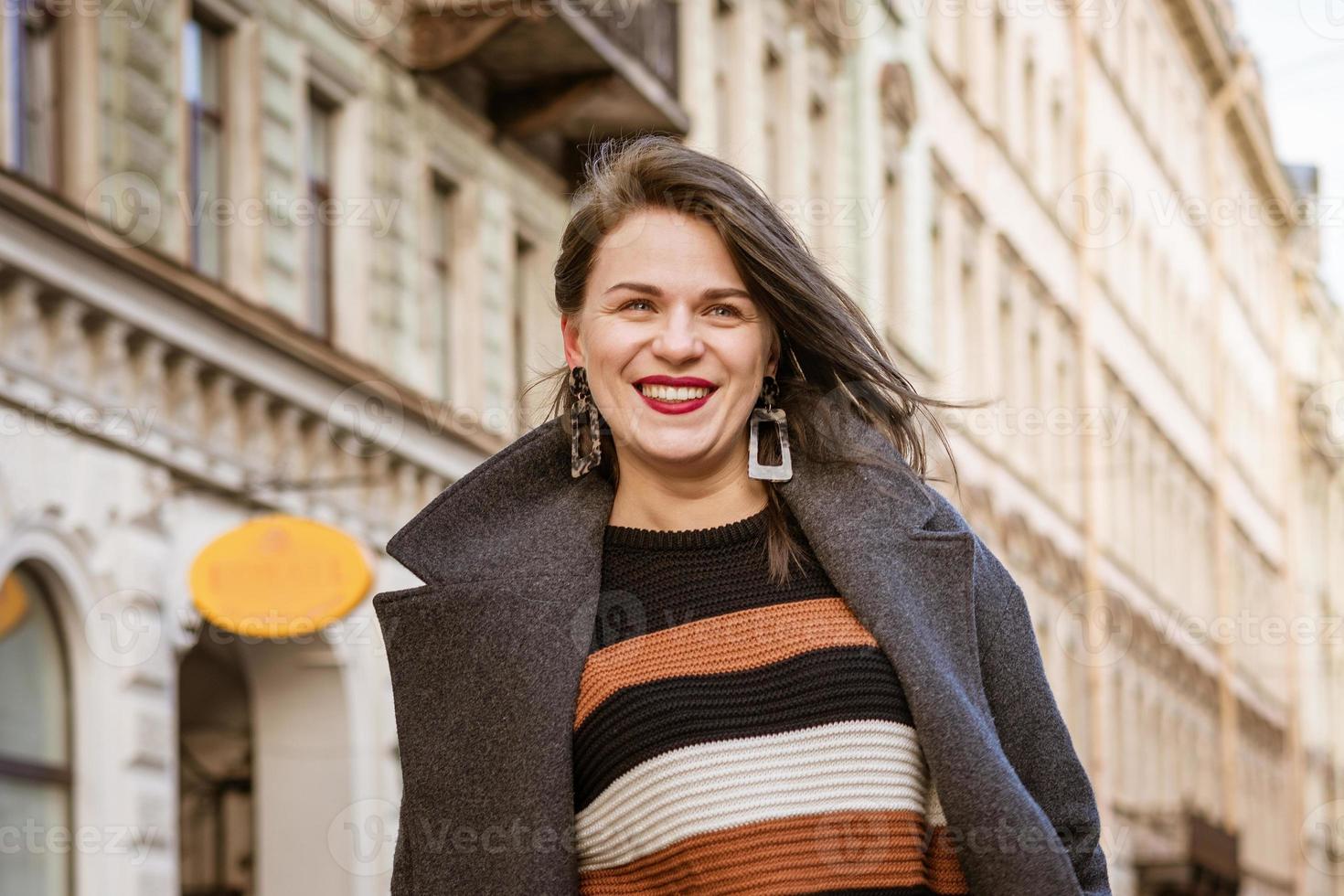gelukkig vrouw in een jas wandelen naar beneden een stad straat foto
