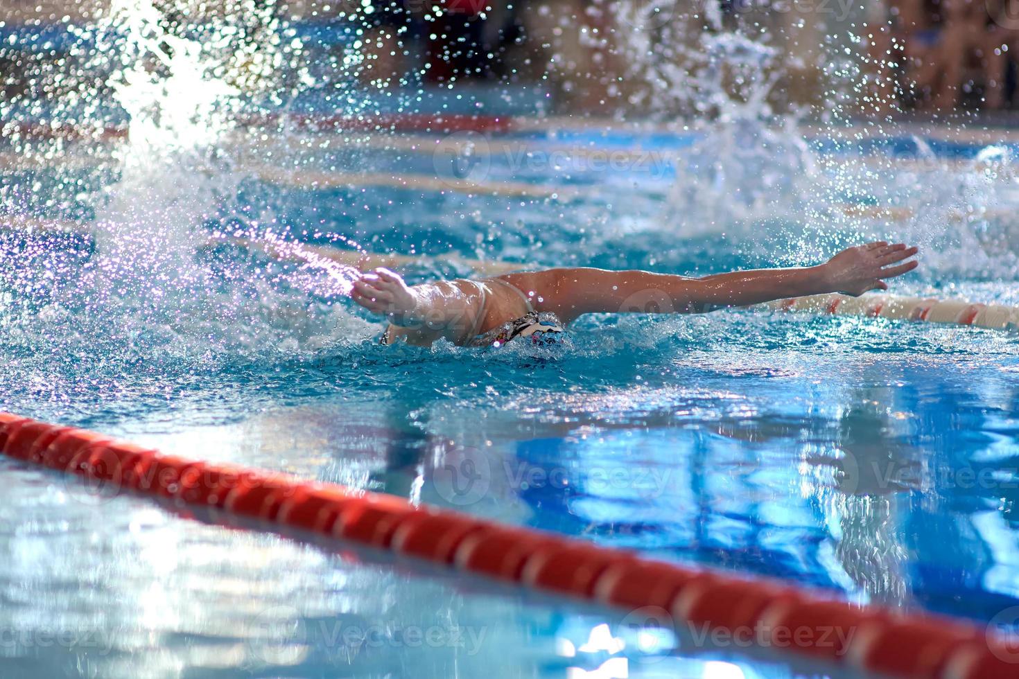 een zwemmer golven zijn armen terwijl het uitvoeren van een vlinder Bij een opleiding sessie in de zwembad, wazig focus foto