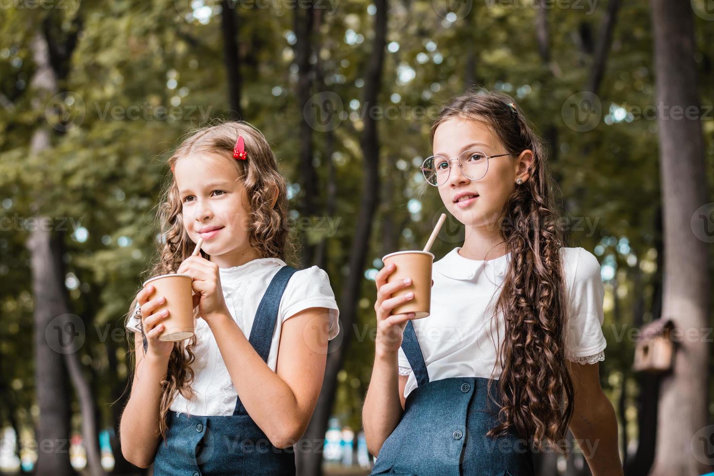 twee schoolmeisjes zijn drinken van milieuvriendelijk cups en drinken rietjes in de park foto