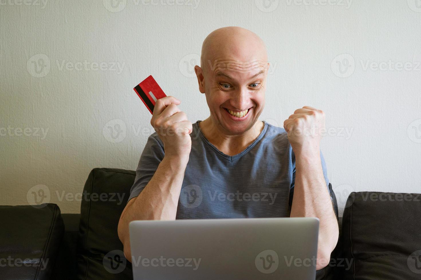 emotioneel kaal Mens Aan sofa met laptop en credit kaart in hand- foto