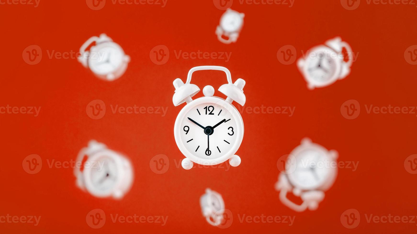 een wit alarm klok in levitatie in de centrum, geïsoleerd Aan een rood achtergrond met een milieu van zweven alarm klokken in de achtergrond. foto