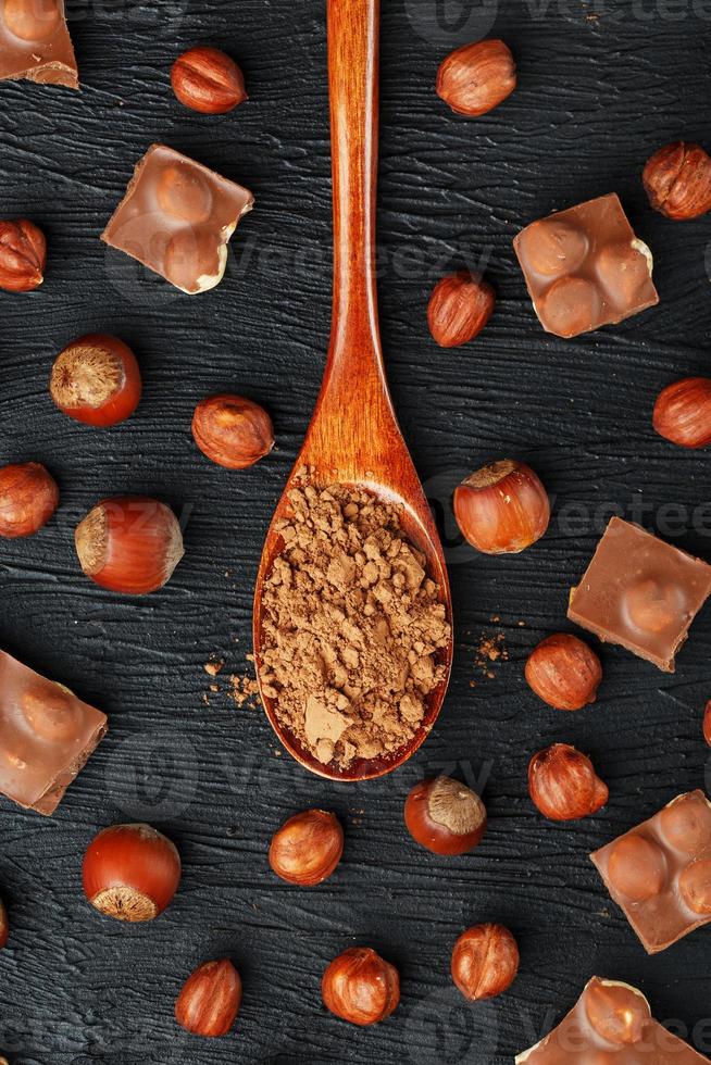 chocola met hazelnoten en een houten lepel met cacao Aan een donker achtergrond, omringd door noten in de schelp en geschild. foto