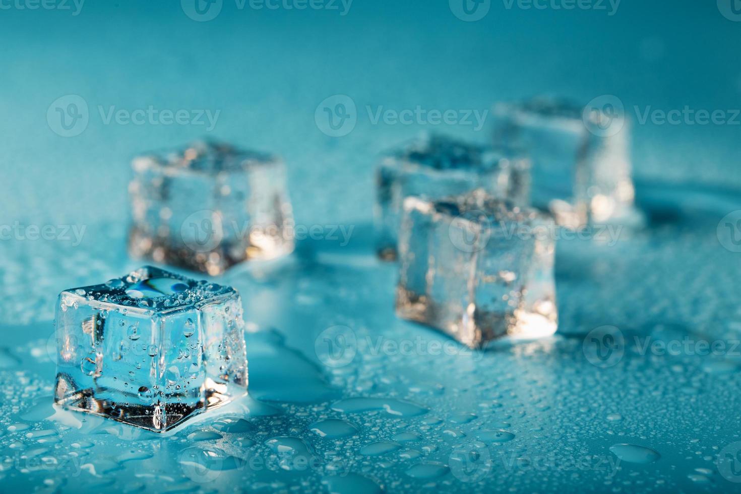 ijs kubussen zijn verspreide met water druppels verspreide Aan een blauw achtergrond. foto