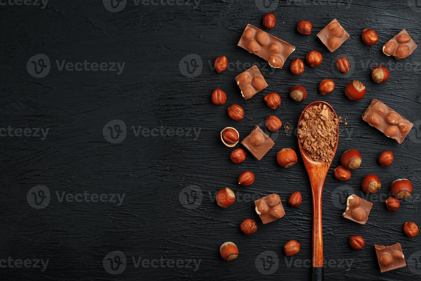 chocola met hazelnoten en een houten lepel met cacao Aan een donker achtergrond, omringd door noten in de schelp en geschild. foto