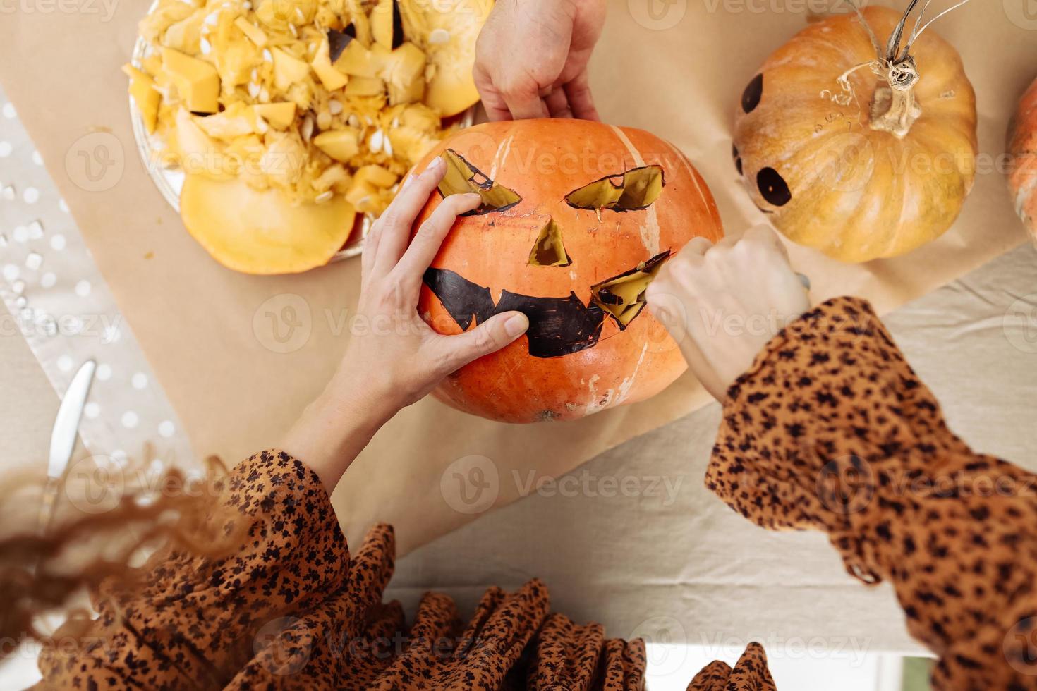 dichtbij omhoog van jong vrouw snijwerk jack O Lattern van rijp oranje pompoen met mes Aan haar houten keuken tafel. vrouw voorbereidingen treffen allemaal heiligen vooravond halloween partij decoraties. achtergrond, kopiëren ruimte. foto