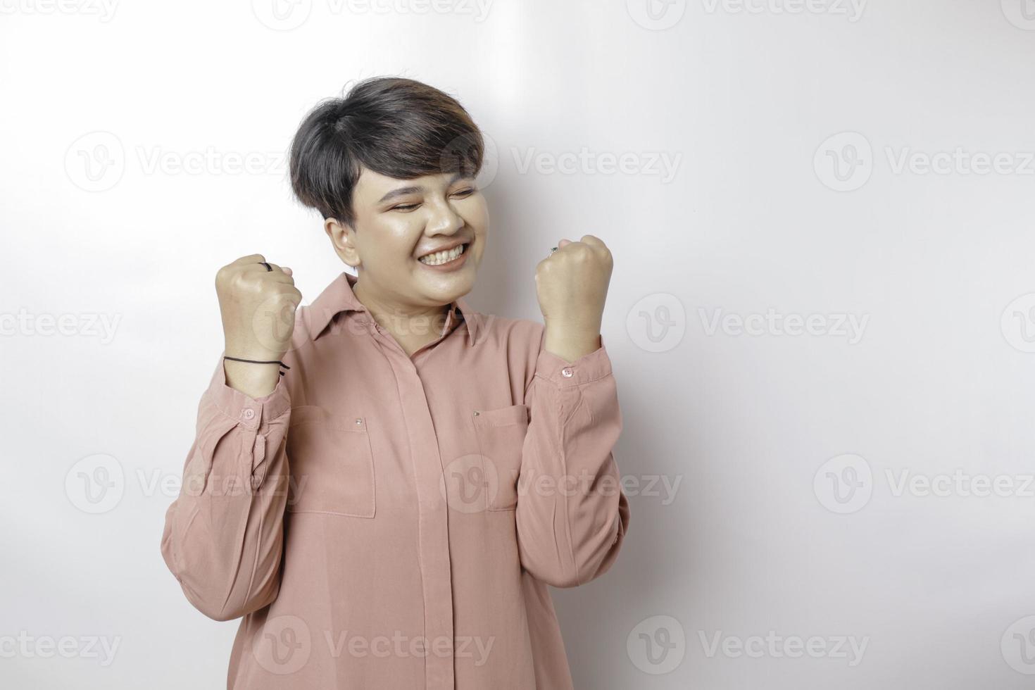 een jong kortharig Aziatisch vrouw met een gelukkig geslaagd uitdrukking vervelend een roze overhemd geïsoleerd door een wit achtergrond foto