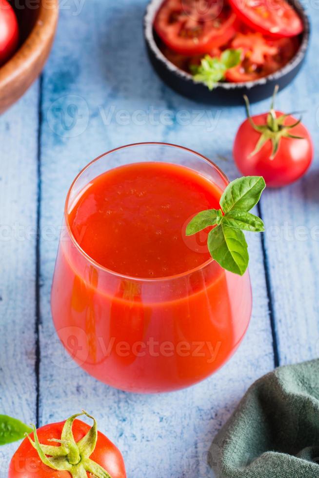 biologisch eigengemaakt tomaat sap met basilicum bladeren in een glas Aan de tafel. verticaal visie foto