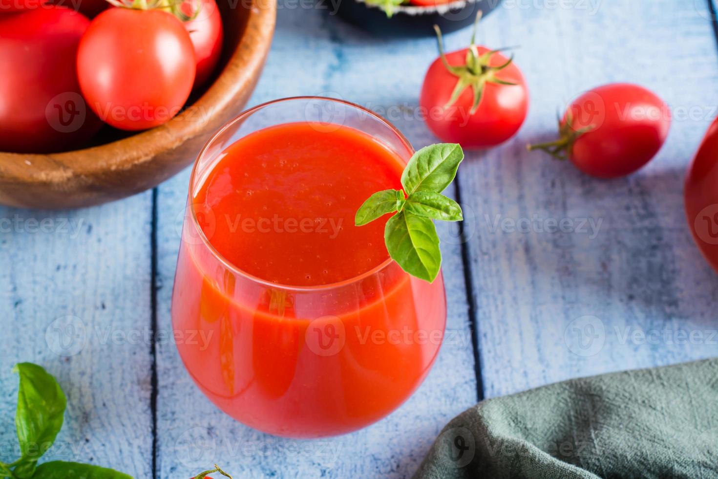 biologisch eigengemaakt tomaat sap met basilicum bladeren in een glas Aan de tafel foto