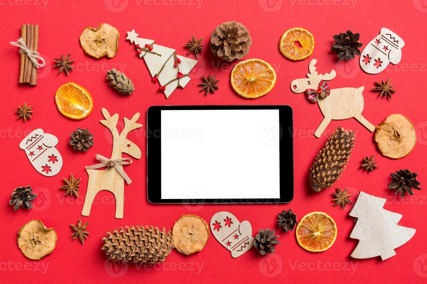 top visie van digitaal tablet, rood achtergrond versierd met feestelijk speelgoed en Kerstmis symbolen rendieren en nieuw jaar bomen. vakantie concept foto