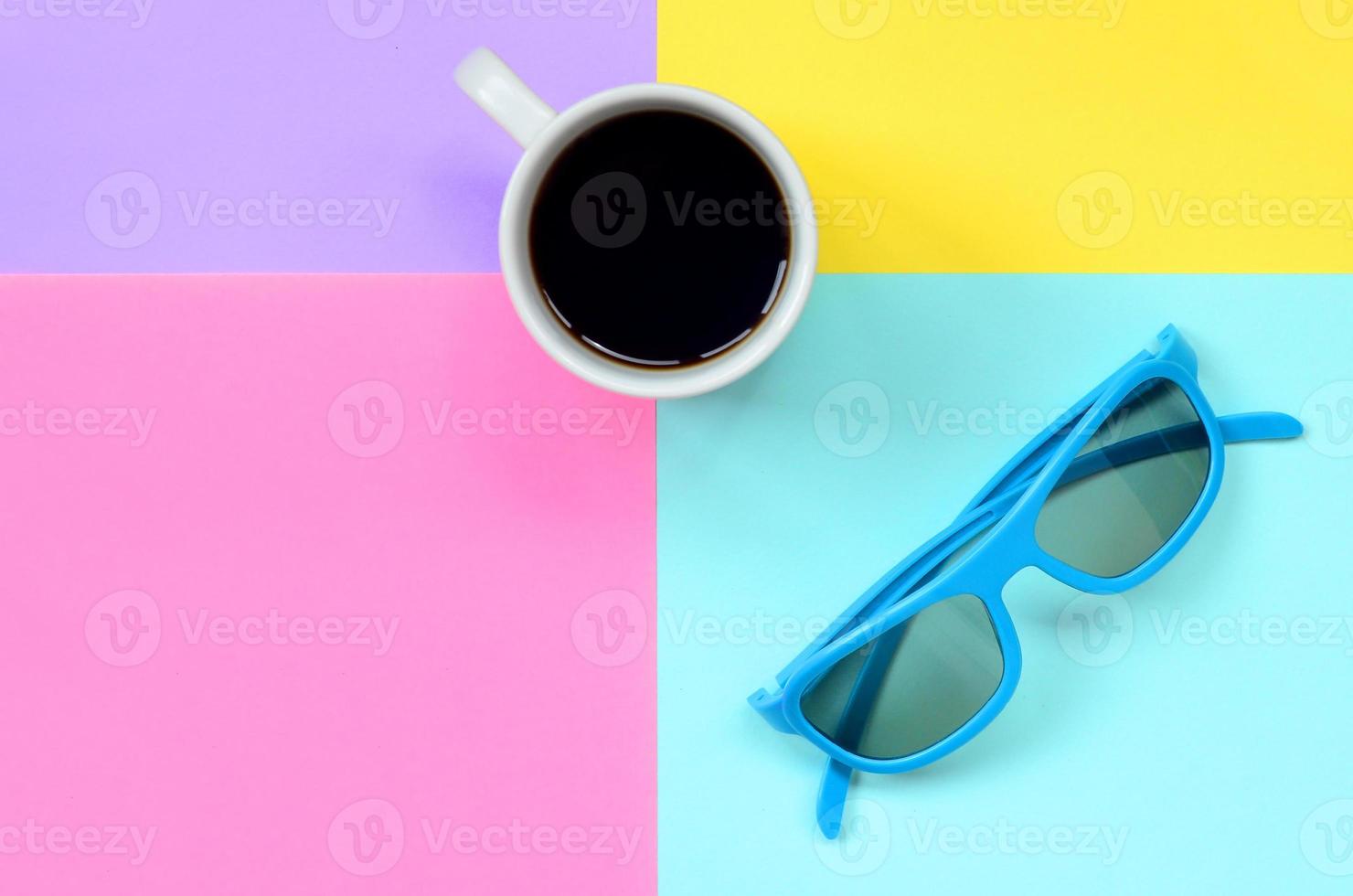 klein wit koffie kop en blauw zonnebril Aan structuur achtergrond van mode pastel blauw, geel, paars en roze kleuren papier in minimaal concept foto