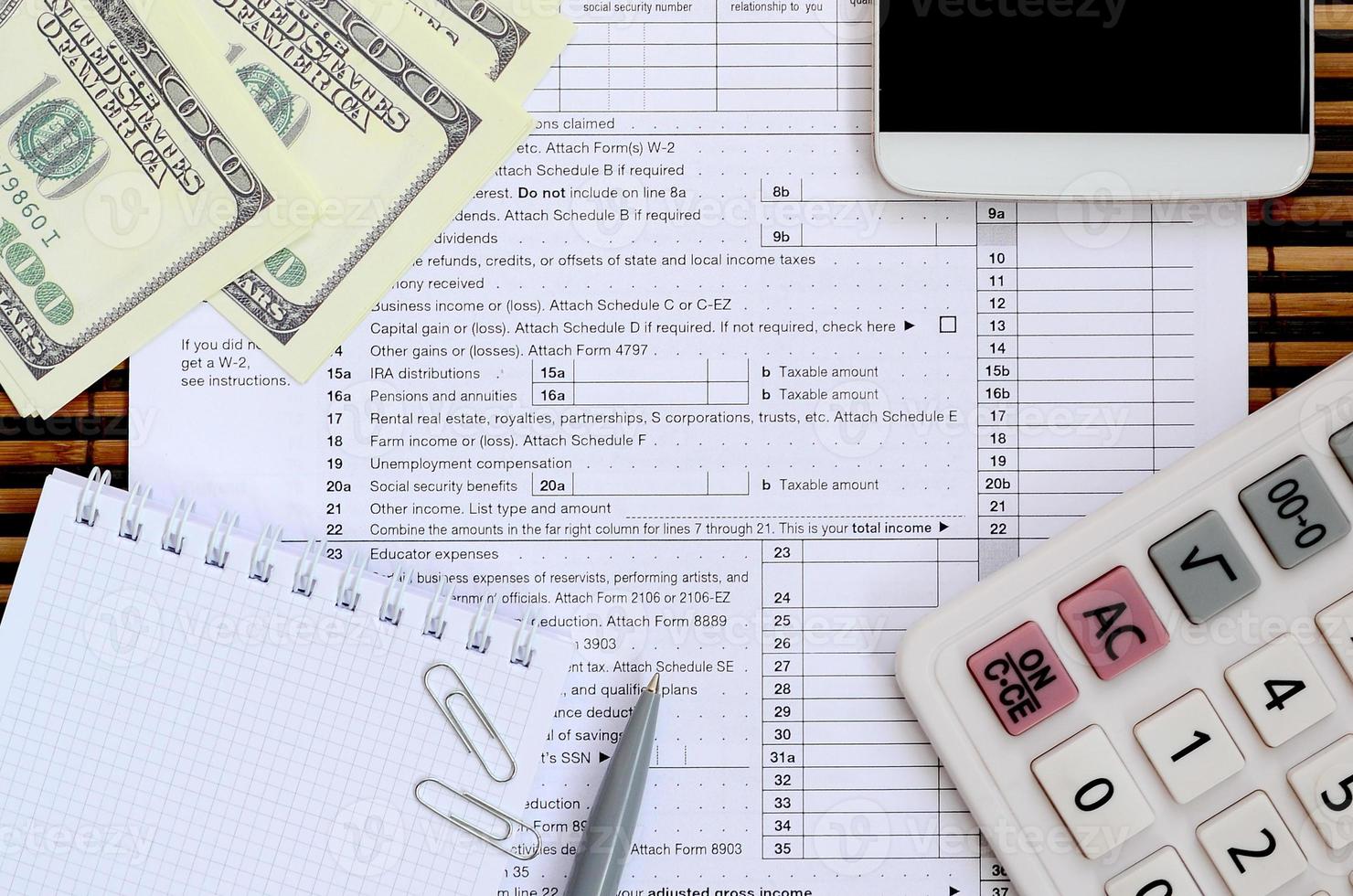 samenstelling van items aan het liegen Aan de 1040 belasting het formulier. dollar rekeningen, pen, rekenmachine, smartphone, papier klem en kladblok. de tijd naar betalen belastingen foto
