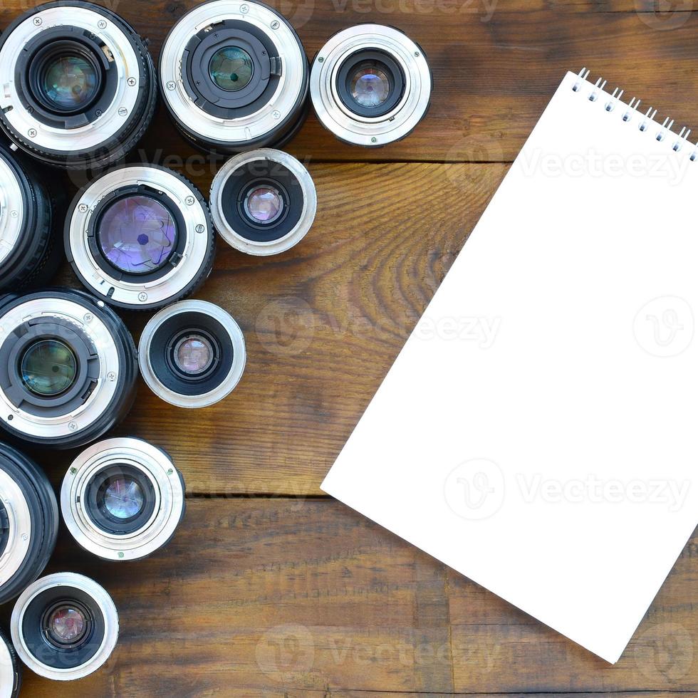 meerdere fotografisch lenzen en wit notitieboekje liggen Aan een bruin houten achtergrond. ruimte voor tekst foto