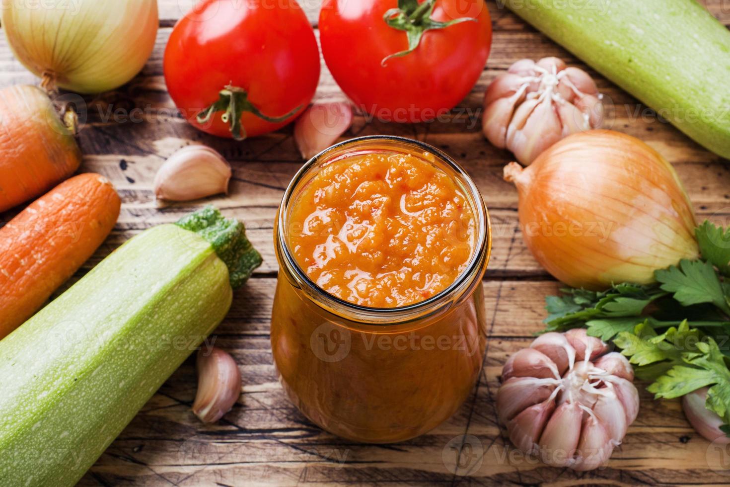 eigengemaakt kaviaar van courgette tomaten en uien in een glas pot Aan een houten achtergrond. eigengemaakt productie inblikken, ingeblikt gestoofd groente. foto