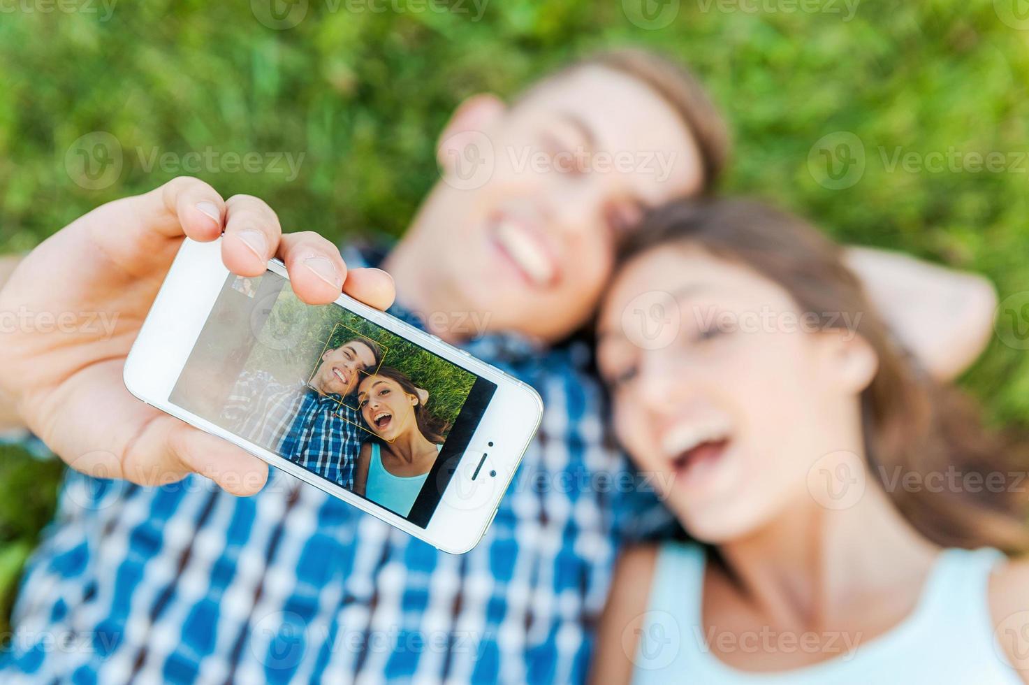 vastleggen de helder emoties. top visie van gelukkig jong liefhebbend paar maken selfie met slim telefoon terwijl aan het liegen Aan de gras. foto