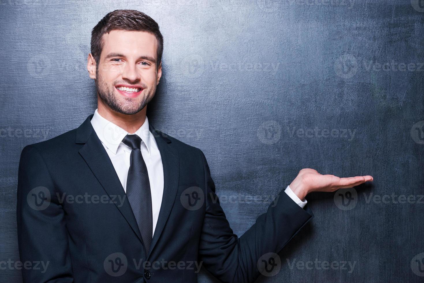 Holding kopiëren ruimte. knap jong Mens in formele kleding op zoek Bij camera en Holding kopiëren ruimte terwijl staand tegen schoolbord foto