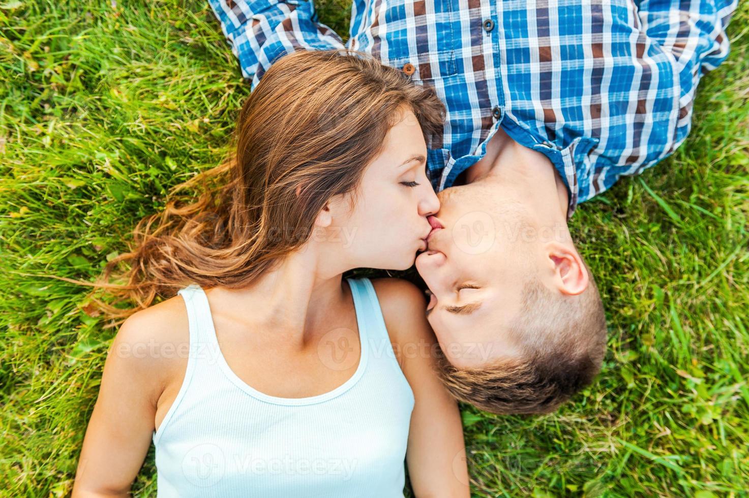 inschrijving kussen. top visie van een jong paar in liefde aan het liegen samen Aan de gras en zoenen foto