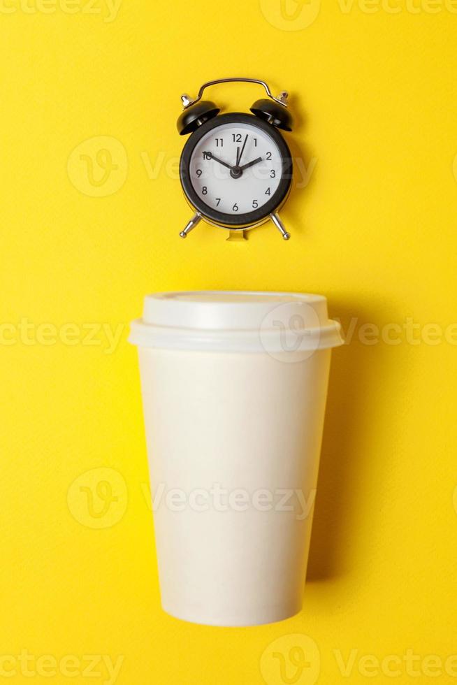 eenvoudig vlak leggen ontwerp papier koffie kop en alarm klok Aan geel kleurrijk modieus achtergrond. meenemen drinken en ontbijt drank. mooi zo ochtend- wakker worden omhoog wakker concept. top visie kopiëren ruimte. foto