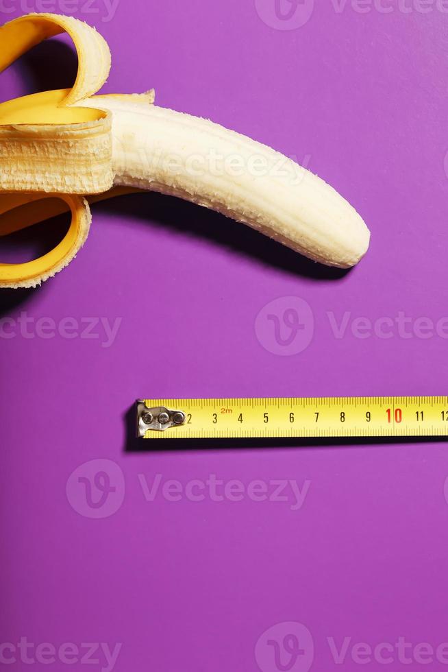 geel banaan penis concept gemeten door meten plakband Aan roze achtergrond. vergelijking van de grootte van een man's waardigheid. foto