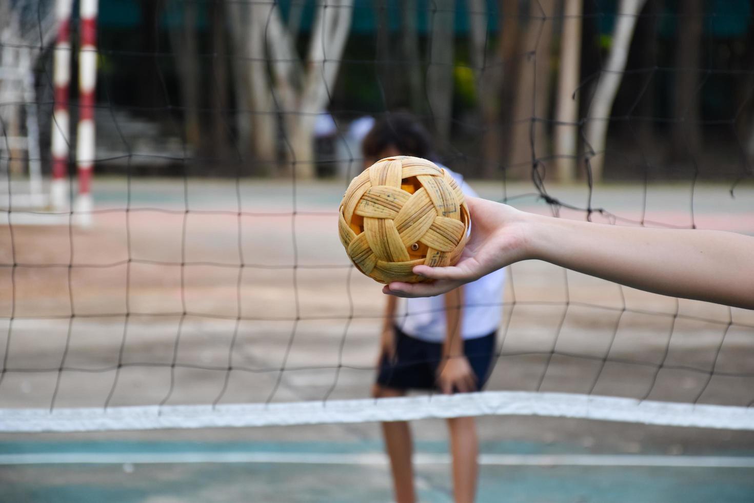 sepak takraw bal, zuidoosten Aziatisch landen traditioneel sport, Holding in hand- van jong Aziatisch vrouw sepak takraw speler in voorkant van de netto voordat het werpen het naar een ander speler naar trap over- de netto. foto